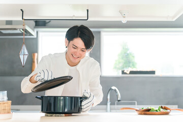 キッチンで鍋の蓋を開ける若い男性（料理教室・手料理・料理男子）
