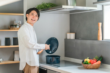 キッチンのHIコンロで煮込み料理をする若い男性（自炊・料理男子）
