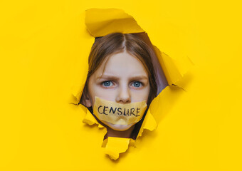 A child with his mouth taped shut peeks through a torn hole in yellow paper.The inscription on the...