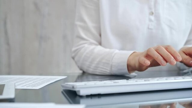 Close-up of a person's hands typing on a white keyboard with papers in background. Business people concept
