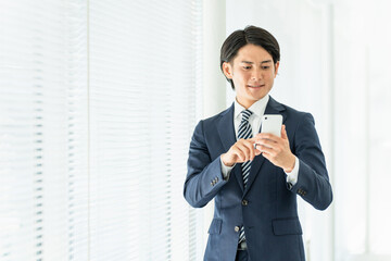 スマートフォンを操作・検索するスーツ姿の若いアジア人ビジネスマン
