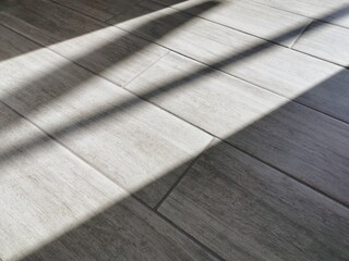 The texture is a pattern of porcelain stoneware tiles on a gray floor with a woody structure with rays of sunlight in the interior