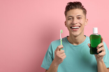 Young man with mouthwash and toothbrush on pink background, space for text