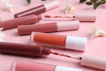 Different lip glosses, applicators and flowers on pink background, closeup - obrazy, fototapety, plakaty