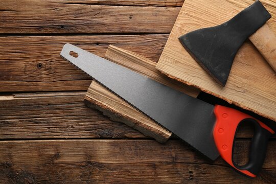 Saw with colorful handle, axe and logs on wooden background, flat lay. Space for text