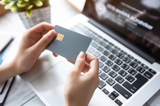Close up of a woman's hands holding a gray credit card in front of a laptop computer