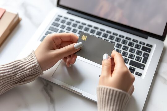 Close up of a woman's hands holding a gray credit card in front of a laptop computer