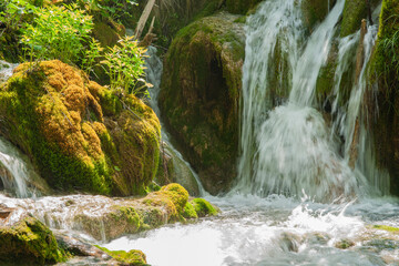 Waterfall over rock and greenery with sun from left through foliage Croatia