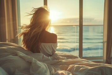 Woman on bed looking out the window overlooking the sea and sunrise
