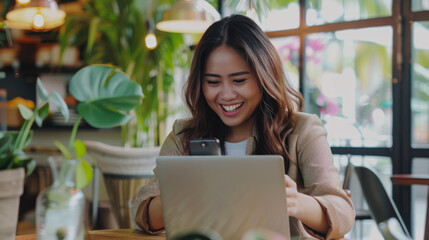 A Filipina entrepreneur happily using her phone in front of her laptop.