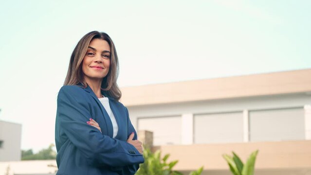 Happy confident mature older Latin business woman real estate agent, saleswoman realtor or new property buyer modern villa owner standing outside villa or country house outdoors. Portrait.
