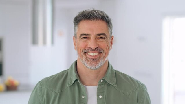 Happy middle aged man with dental smile standing looking at camera at home. Confident mature senior man, 50 years old handsome man real estate owner in modern house living room. Close up face portrait