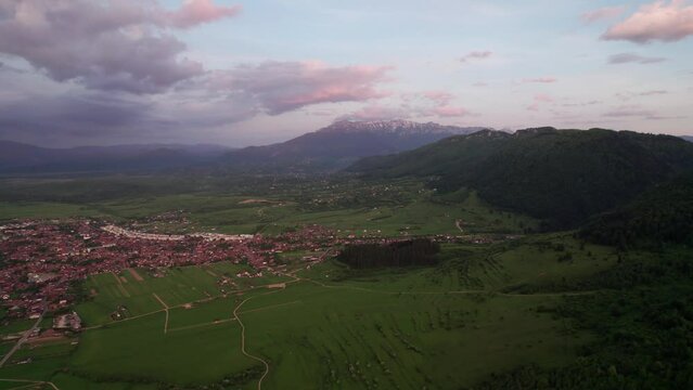 Zarnesti city near bucegi mountains at sunset with vibrant sky and green fields, aerial view