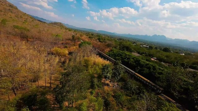 FPV drone shot approaching a train in Thailand with a forest and blue skies all around