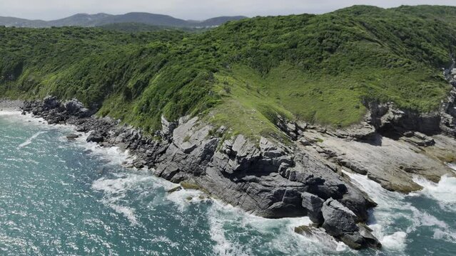 Drone flies up and away from rocks on edge of coast