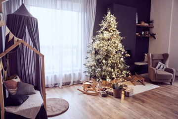 Christmas decor in domestic, cosy living room with christmas tree with lighting strings, wooden rocking chair, gifts, bed with canopy, armchair. Background with copy space. Concept of Christmas.
