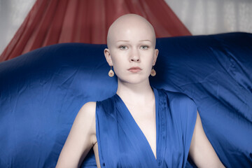 A frontal close-up of a bald model in a blue dress, showing a thoughtful expression with a bold...