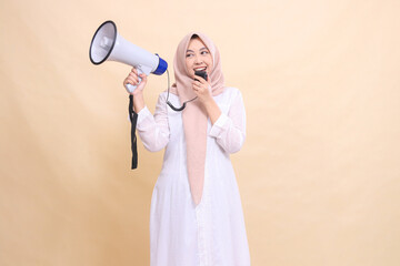woman asian mature wearing a candid hijab shouts cheerfully holding a loudspeaker megaphone and holding the speaker mic near her mouth. Technology, broadcast and promotion concept