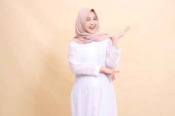 girl asian muslim standing to the camera smile cheerful wink eyes crossed arms presenting to the left. Fashion, pointer, business and promotion concept