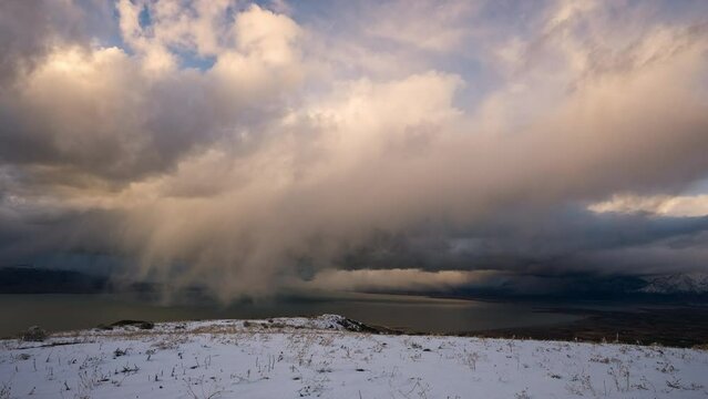 Storm moving in timelapse over Utah Lake during sunset looking past snowy landscape.