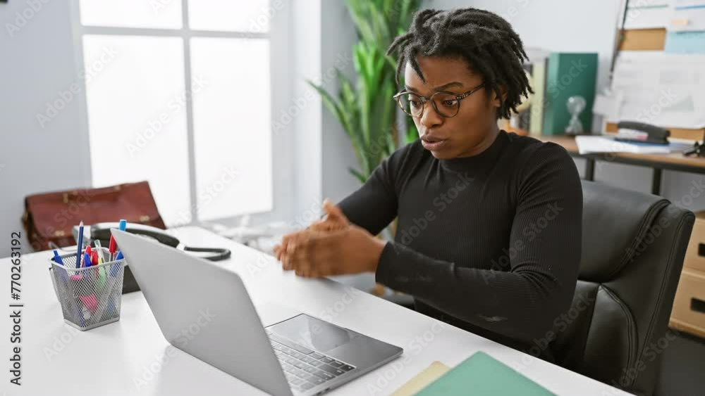 Sticker Focused african american woman with dreadlocks working on laptop in modern office setting.