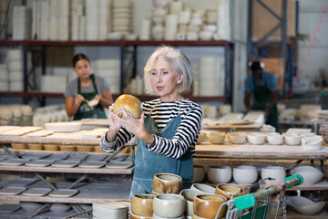 Senior woman ceramist arranging new bowls in workshop. Photo of skillful female handicraft worker.