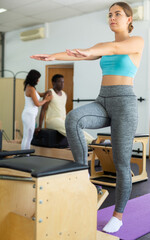 Fototapeta na wymiar Young girl performing set of pilates exercises on reformer in modern fitness studio