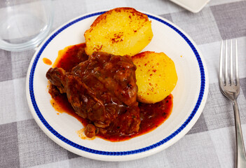 Delicious fried pork cheeks served in sauce with baked potatoes on plate