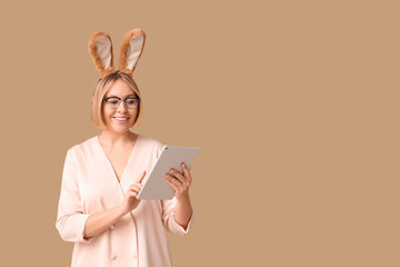 Happy adult businesswoman in bunny ears with tablet computer on beige background. Easter celebration