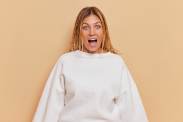Woman in white sweater shows surprise with open mouth, arms, and happy gesture