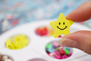 Fingers Holding a Smiling Star Wooden Bead for Making Beaded Accessories