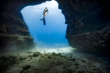 A female free diver returns to the surface from an underwater cave opening in the clear blue waters...