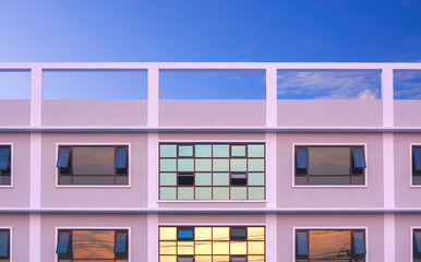 Geometric architecture minimal background of modern office building with sunset sky reflection on many glass windows surface with rooftop against blue sky in evening time