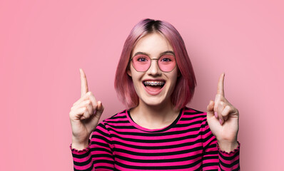 Excited pink haired woman in braces, opened mouth, wear sunglasses glasses spectacles advertise...