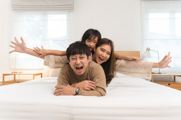 Happy Asian family, young father, mother, cute daughter lying together on bed in bedroom at home....