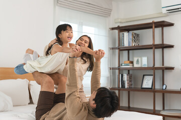Happy Asian family, father, mother, cute daughter playing on bed in bedroom at home, bond and relax...