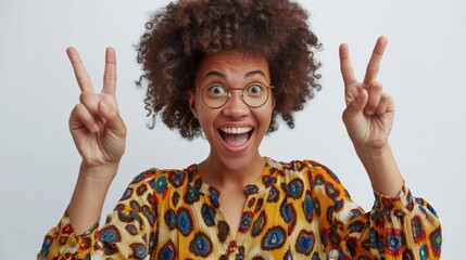 Woman with curly hair making peace sign gestures. A jubilant woman with curly hair gives peace signs, smiling widely with round glasses, against a white backdrop