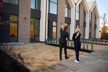 Back view picture of client and realtor walking near buildings