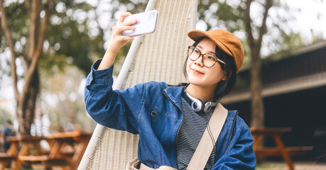 Young asian woman using smartphone for selfie wearing hat denim jacket music headphone and...