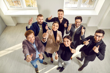 Happy business team giving thumbs up all together. Cheerful young people standing in office,...