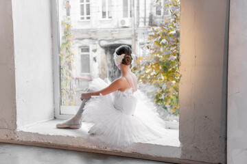 Ballerina sits thoughtfully by a sunlit window, her gaze outward, surrounded by urban decay and...
