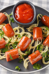 Delicious spaghetti hot dog in the form of spiders and ketchup close-up in a plate on the table. Vertical top view from above
