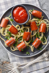 Festive funny food spaghetti with sausages and ketchup close-up in a plate on the table. Vertical top view from above