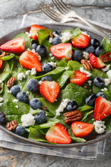 Spring salad of spinach, strawberries, blueberries, goat cheese and pecans close-up in a plate on the table. Vertical