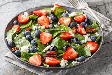 Spinach salad with strawberries, blueberries, cheese and pecans with honey dressing close-up in a plate on the table. Horizontal
