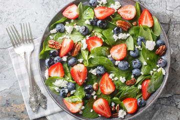 Spinach salad with strawberries, blueberries, cheese and pecans with honey dressing close-up in a plate on the table. Horizontal top view from above