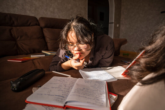 Asian young woman in glasses preparing for exams home on couch