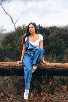 Young woman sitting on log on hiking trail looking to background