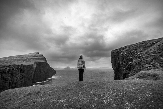 Black and white image of woman standing alone at edge of cliff.
