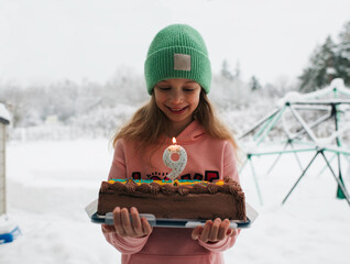 9 year old girl looking at her birthday cake with a candle